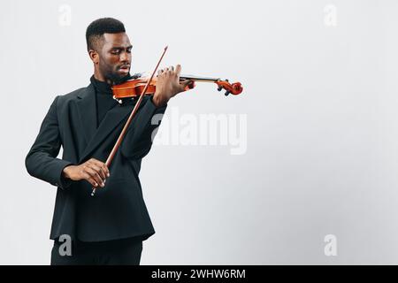 Giovane afroamericano di talento in elegante abito nero che suona violino con passione, isolato su sfondo bianco Foto Stock