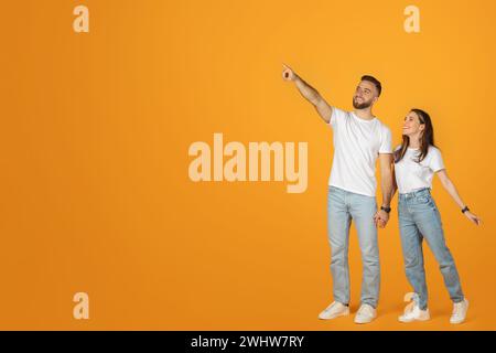 Un uomo e una donna adorabili con i top bianchi e i jeans blu che si tengono per mano e puntano verso l'alto Foto Stock