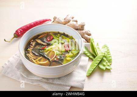 Zuppa piccante di verdure asiatiche con spaghetti, miso, alghe nori, zenzero e peperoncino in una ciotola su un tavolo di legno, copia spazio, selezionato Foto Stock