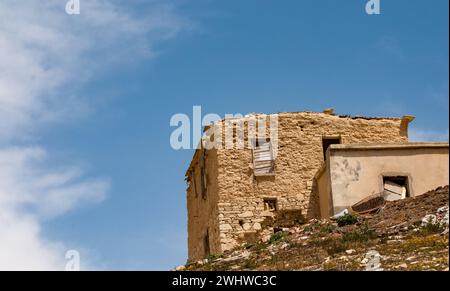 Casa abbandonata in argilla deserta ai margini della scogliera. Rovine di un vecchio villaggio abbandonato. Spazio copia cielo blu Foto Stock