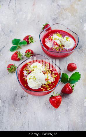 Tradizionale zuppa di fragole surgelata con gelato alla vaniglia e pistacchi schiacciati servita come primo piano su una tavola di design con tex Foto Stock