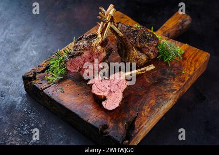 Tradizionale griglia di agnello alla griglia con erbe aromatiche servita come primo piano su un rustico pannello di legno Foto Stock