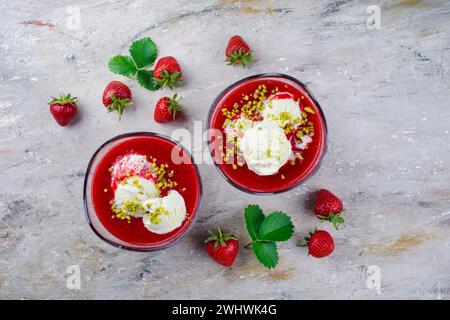 Tradizionale zuppa di fragole surgelata con gelato alla vaniglia e pistacchi schiacciati servita come vista dall'alto su una tavola di design con tex Foto Stock