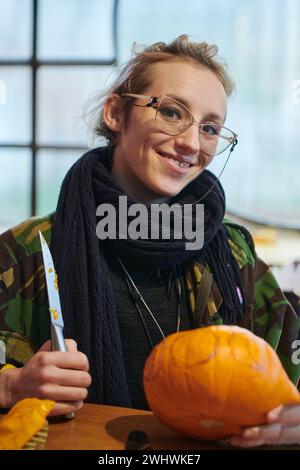 Una moderna donna bionda in uniforme militare sta intagliando zucche spaventose con un coltello per la notte di Halloween Foto Stock