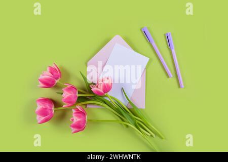 Tulipani rosa con biglietto di auguri e busta su sfondo verde Foto Stock
