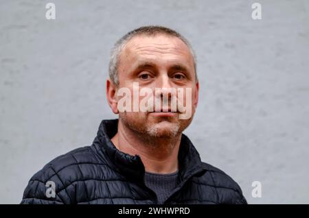 Un uomo anziano dai capelli grigi di 45-50 anni contro una parete di colore chiaro con una giacca nera guarda la fotocamera. Foto Stock
