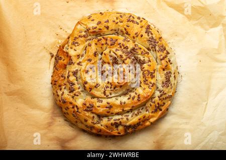 Burek appena sfornato in pasta filla con ripieno su carta da forno vista dall'alto. Tradizionale torta a spirale di Balka Foto Stock