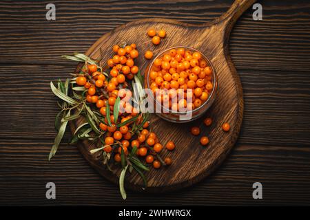 Frutti di bosco maturi in vaso di vetro e rami con vista dall'alto delle foglie su sfondo rustico in legno scuro, perfetto per la pelle, ascolta Foto Stock