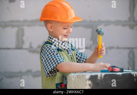 Bambino in casco protettivo arancione con strumenti per la ristrutturazione. Riparazione a casa. Foto Stock