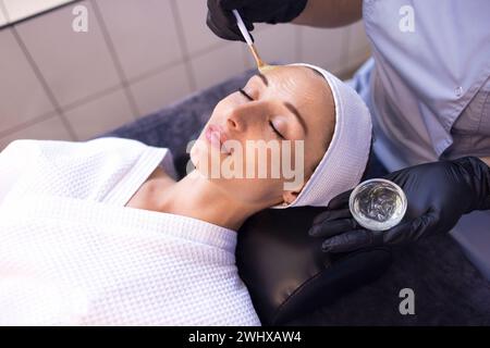 Il maestro di bellezza applica una maschera ringiovanente al viso dei clienti Foto Stock