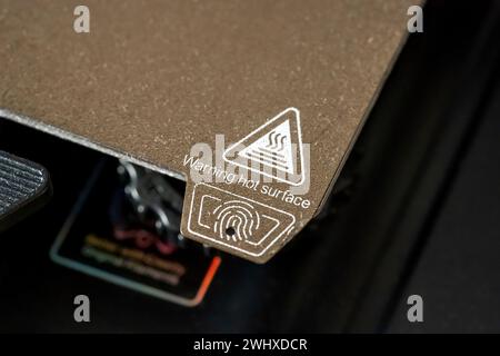 Un'etichetta di avvertenza per superficie calda di un tappetino riscaldato per stampante 3D vista da vicino, nessuno. Apparecchiature e accessori per la stampa 3D concetto semplice, dispositivo Foto Stock