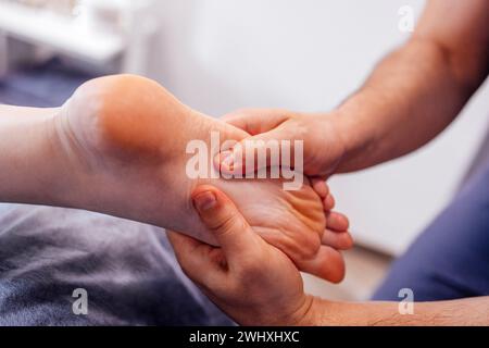 Primo piano del piede femminile con un massaggio delicato. La massaggiatrice tiene la gamba della donna nelle sue mani. Un giovane cliente mente e ama rilassarsi con un professionista Foto Stock