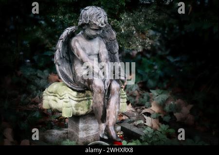 un piccolo angelo con le ali siede tristemente addosso su un cuscino di pietra in una lapide in un cimitero Foto Stock