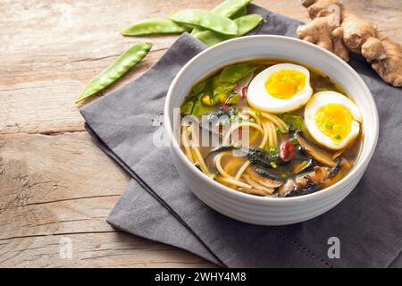 Zuppa di miso con spaghetti, alghe nori, piselli delle nevi, zenzero e uovo in una ciotola su un rustico tavolo di legno, spazio per copiare, focu selezionata Foto Stock