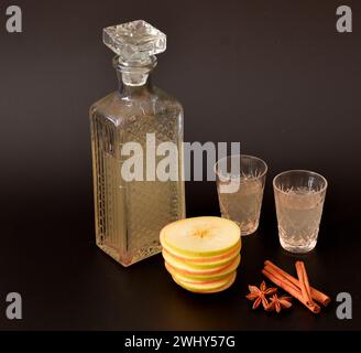 Liquore di mele con cannella e anice su sfondo nero, forte alcol fatto in casa con spezie in una ciotola di cristallo. Primo piano. Foto Stock