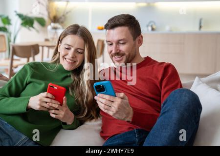 Coppia sorridente seduta con i telefoni cellulari, videochiamata di gruppo con gli amici, gioco online Foto Stock