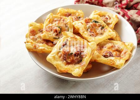 Quadrati di pasta sfoglia al forno con prosciutto, spinaci e formaggio in una ciotola bianca, snack finger food per una festa calda o fredda a buffet, copia Foto Stock