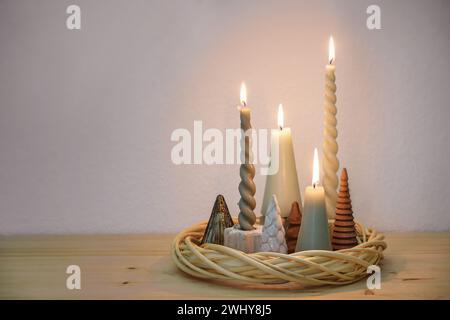 Semplice decorazione dell'avvento in colori naturali con diverse candele e piccoli alberi di Natale artificiali disposti in una corona da Foto Stock