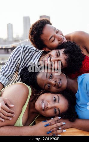 Quattro amici multietnici si mettono la testa sopra l'un l'altro. Giovani di razza mista sullo sfondo di una grande città. Foto Stock