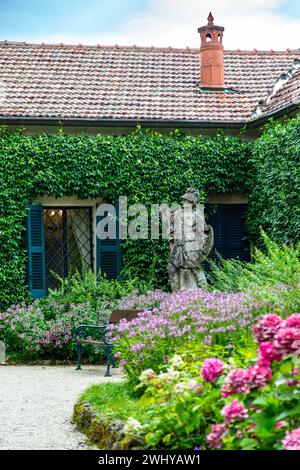 Una statua di un guerriero guarda fuori da un giardino fiorito d'angolo mentre custodisce questo edificio presso Villa del Balbianello a Lenno, in Lombardia, in Italia. Foto Stock