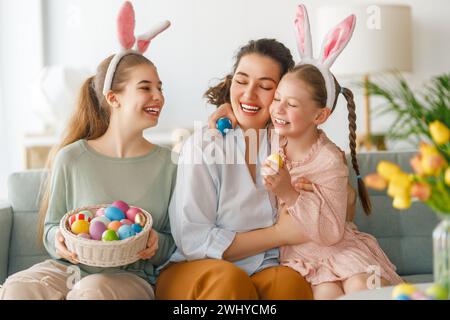 Buona vacanza. Madre e le sue figlie con uova da pittura. La famiglia festeggia la Pasqua. Le ragazze cute dei bambini stanno portando le orecchie conigliate. Foto Stock