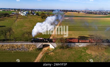 Vista aerea laterale di un treno a vapore che viaggia attraverso le fattorie soffiando fumo Foto Stock