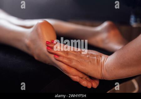 Primo piano del piede femminile con un massaggio delicato. La massaggiatrice tiene la gamba della donna nelle sue mani. Un giovane cliente mente e ama rilassarsi con un professionista Foto Stock