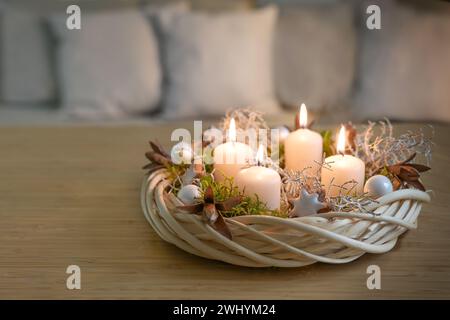 Corona dell'Avvento fatta in casa in vimini in tonalità naturali con candele beige, muschio e decorazioni natalizie su un tavolo in legno Foto Stock