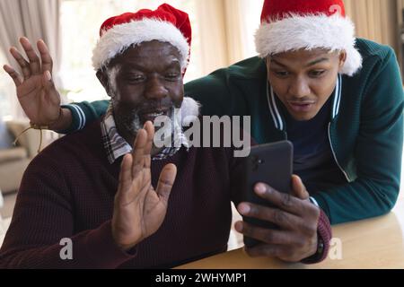 Felice padre e figlio afro-americano nei cappelli di natale con videochiamata su smartphone Foto Stock