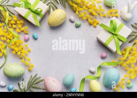 Questa immagine cattura l'essenza della Pasqua con uova color pastello, scatole regalo adornate con nastri verdi e decorazioni gialle vivaci su un morbido Foto Stock