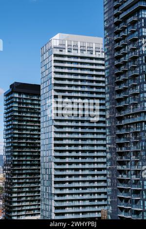 Edifici alti e moderni con facciate di vetro sotto un cielo azzurro che riflette la luce del sole. Foto Stock