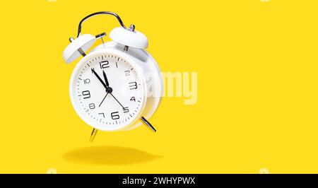 Sveglia con campana bianca su sfondo giallo. concetto di clock da 5 a 12 isolato. Foto Stock