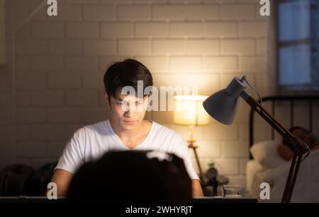 Giovane, attraente e felice uomo asiatico che lavora su un computer portatile a casa per il successo aziendale e il concetto di imprenditore Foto Stock