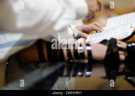 Giovane che pratica la lettura della Torah prima della celebrazione di Bar Mitzvah. Indossare Tefillin sulla mano destra. Foto Stock