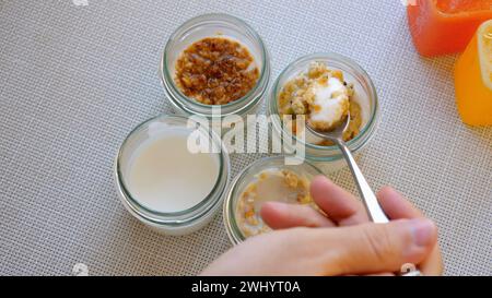 Una persona sta tenendo un cucchiaio davanti a quattro vasetti di cibo Foto Stock