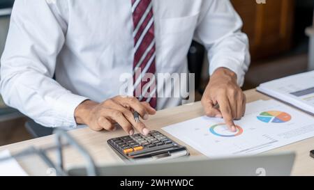 Commercialista che analizza i grafici di investimento fattura e premendo i pulsanti della calcolatrice sui documenti. Contabile Foto Stock