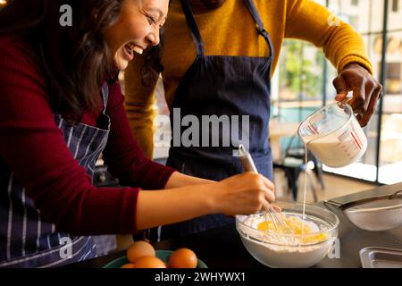 Allegri coppie che preparano i biscotti natalizi mescolando l'impasto in cucina Foto Stock