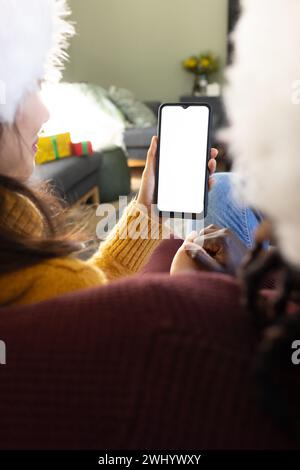 Felice coppia variegata nei cappelli di natale con videochiamata su smartphone, schermata spazio copia Foto Stock