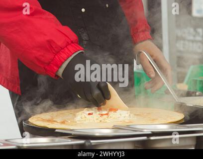 Corpo di un uomo che prepara pancake o crepes francesi con formaggio e prosciutto al mercato del cibo di strada degli agricoltori sul lungomare di Naplavka a Praga, Repubblica Ceca Foto Stock