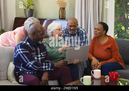 Felice gruppo di amici anziani che utilizzano un notebook per discutere nel soggiorno soleggiato Foto Stock