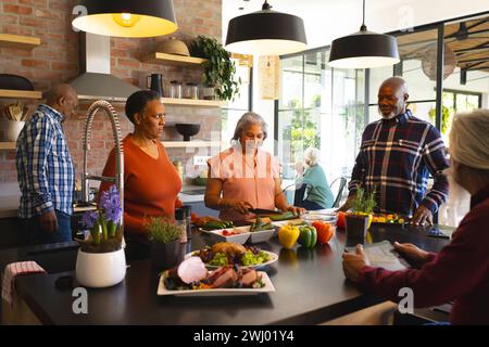 Felice gruppo di amici anziani che preparano il pasto nella cucina soleggiata di casa Foto Stock