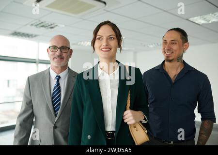 Giovane e felice azienda donna leader nel settore dell'abbigliamento formale che si muove avanti con due colleghi o subordinati interculturali di sesso maschile Foto Stock
