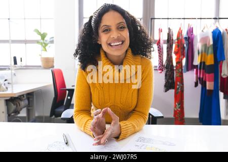 Felice stilista birazziale che ha videochiamato e ride alla scrivania in studio. Moda, design, creatività, abbigliamento e piccole imprese, com Foto Stock