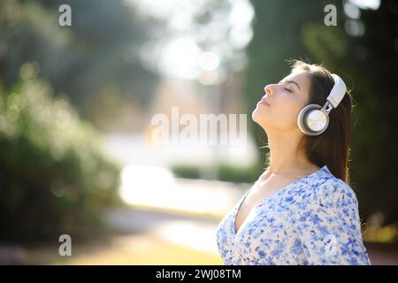 Profilo di una donna che respira aria fresca e che medita ascoltando l'audioguida sulle cuffie in giardino Foto Stock