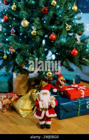 Santa figurine si trova vicino a regali colorati giacenti sul pavimento sotto l'albero di Natale Foto Stock