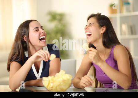 Due amici felici che ridono divertentissimo mangiando patatine fritte a casa Foto Stock