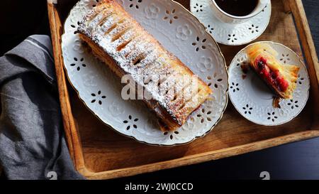 Tradizionale strudel di mele intero appena sfornato su un tavolo di legno, primo piano. Pasticcini freschi fatti in casa con ripieno di frutta o frutti di bosco Foto Stock