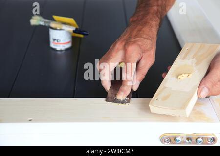 Coltello per stucco in mano all'uomo. Lavoratore fai da te che applica il riempitivo al legno. Rimozione dei fori da Foto Stock