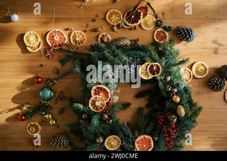 Pezzi di arance secche, giocattoli e coni di abete si trovano vicino alla corona di Natale sul pavimento Foto Stock