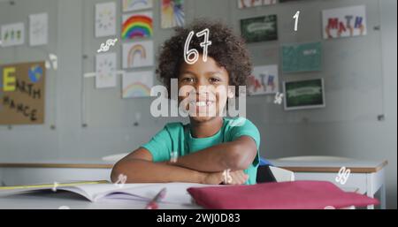 Immagine di numeri su felice scolaro birazziale seduto alla scrivania in classe sorridente Foto Stock